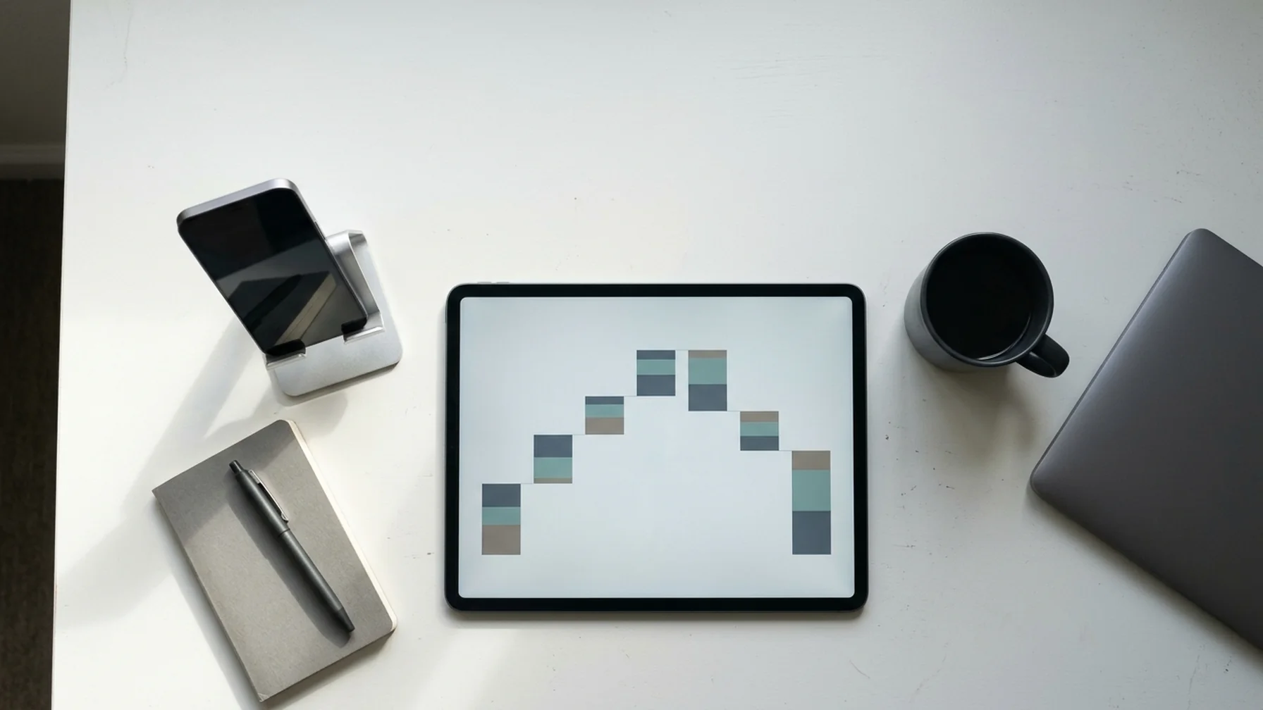 Developer desk with a tablet showing an ad waterfall diagram beside a phone propped on a stand, daylight from the side